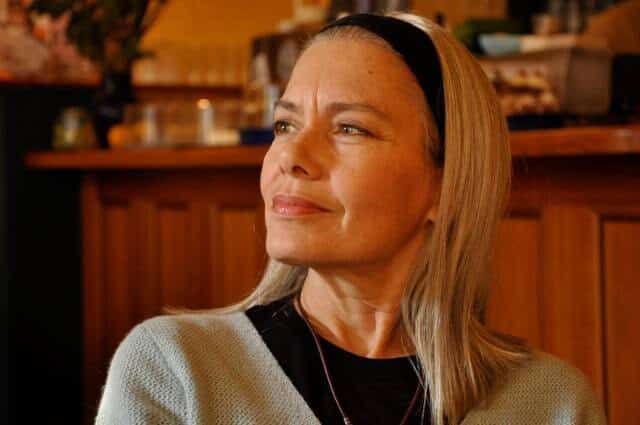 Candida Royalle, capelli biondi e cerchietto nero, pensierosa e sorridente in un caffè